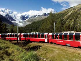Panoramabild des Glacier Express auf grünen Hügeln vor schneebedeckten Bergen